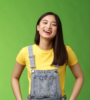 Carefree enthsuastic outgoing attractive teenage asian girl having fun laughing friends, hold hands overalls pockets smiling toothy, take party easygoing conversation, stay positive green background