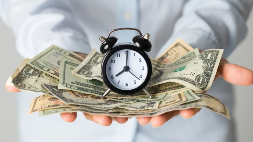 small clock on top of dollar bills small clock on top of dollar bills